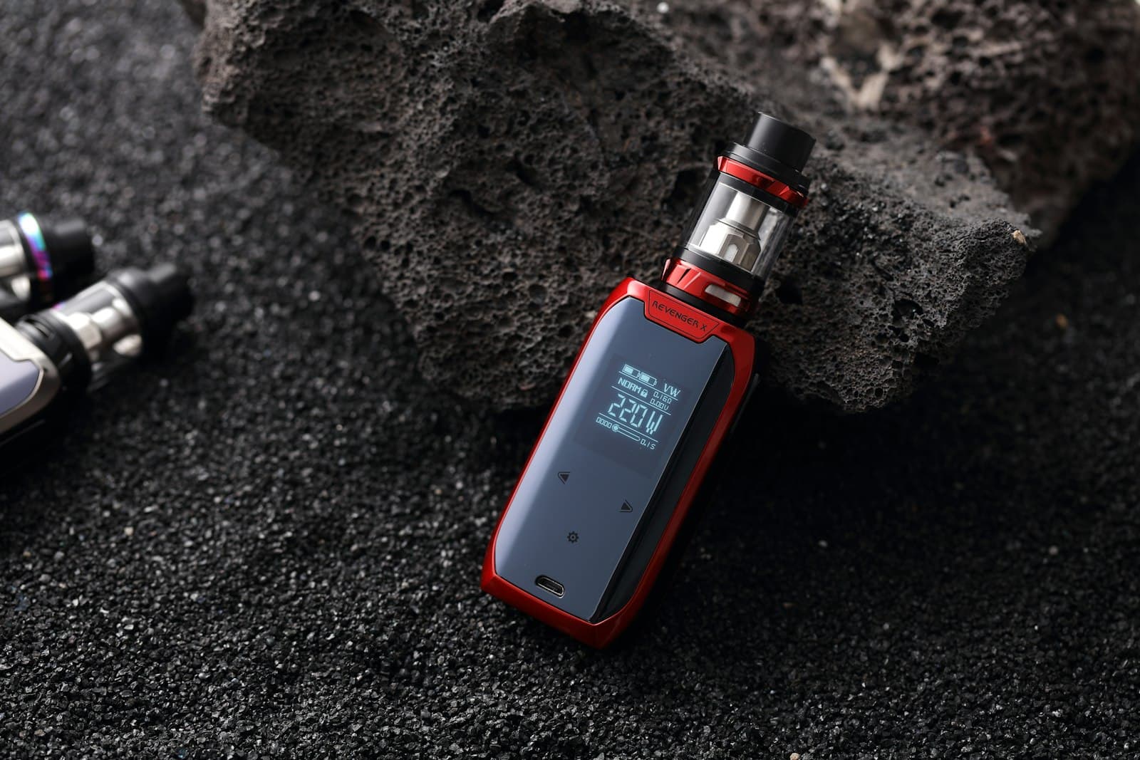 Close-up of a red and black box mod kit's zinc-alloy chassis and screen resting against dark volcanic rock
